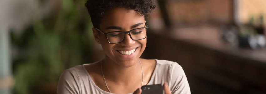 A woman smiling as she looks at her phone screen